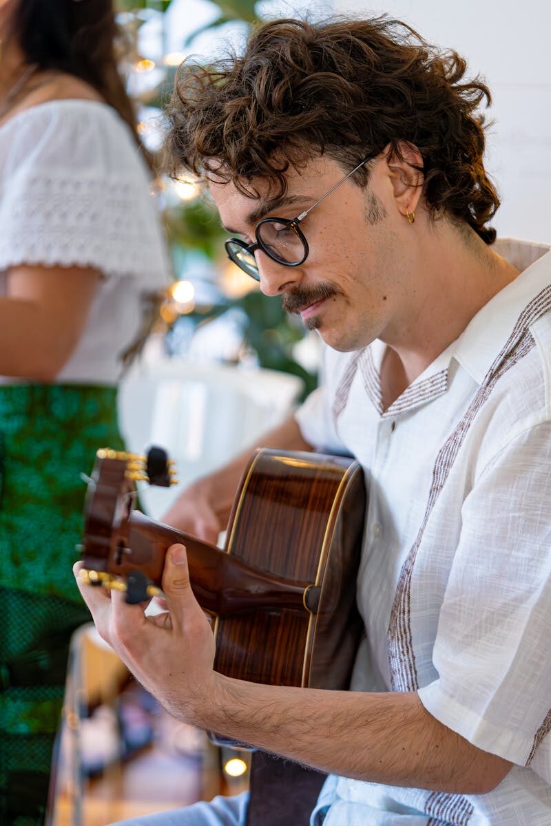 A focused young adult man plays an acoustic guitar indoors, showcasing musical passion.